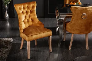 Estila Designová chesterfield jídelní židle Torino hořčicově žluté barvy ze sametu s dřevěnými nohami a stříbrným klepadlem 96cm